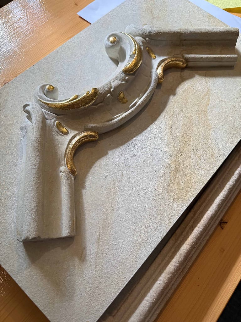 Ornamentale Gipsverzierung mit Goldakzenten auf Holz.